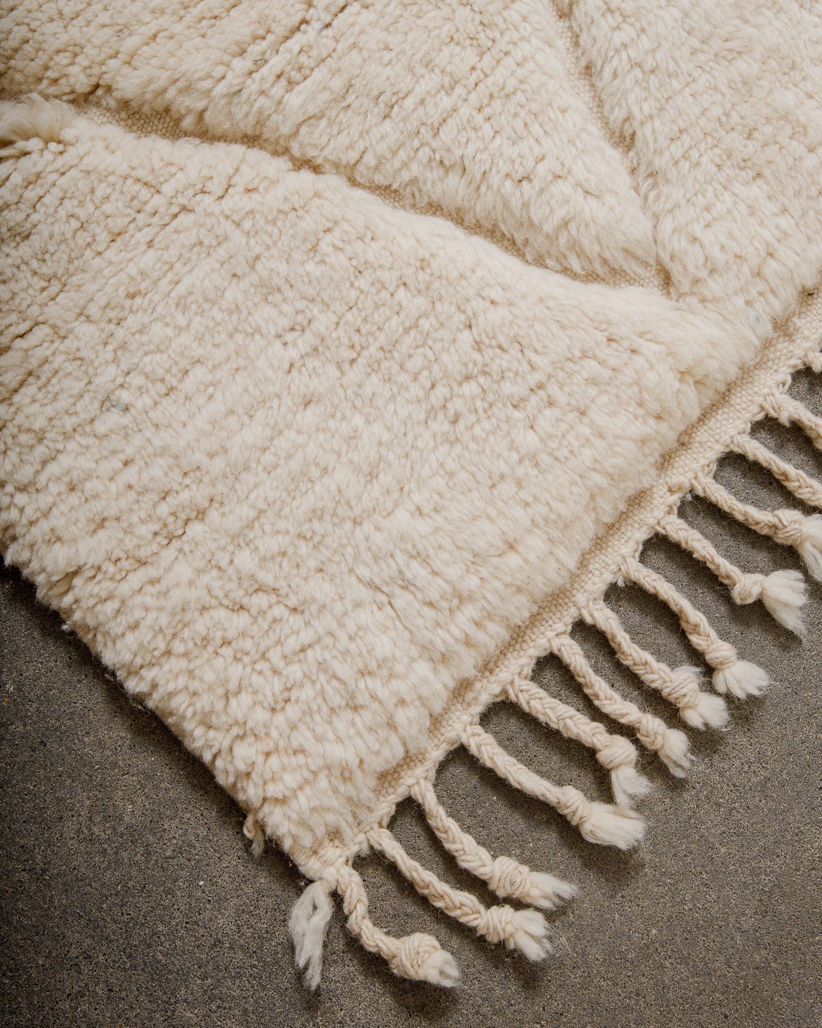 Corner of a cream wool rug with natural wool tassels on concrete floor